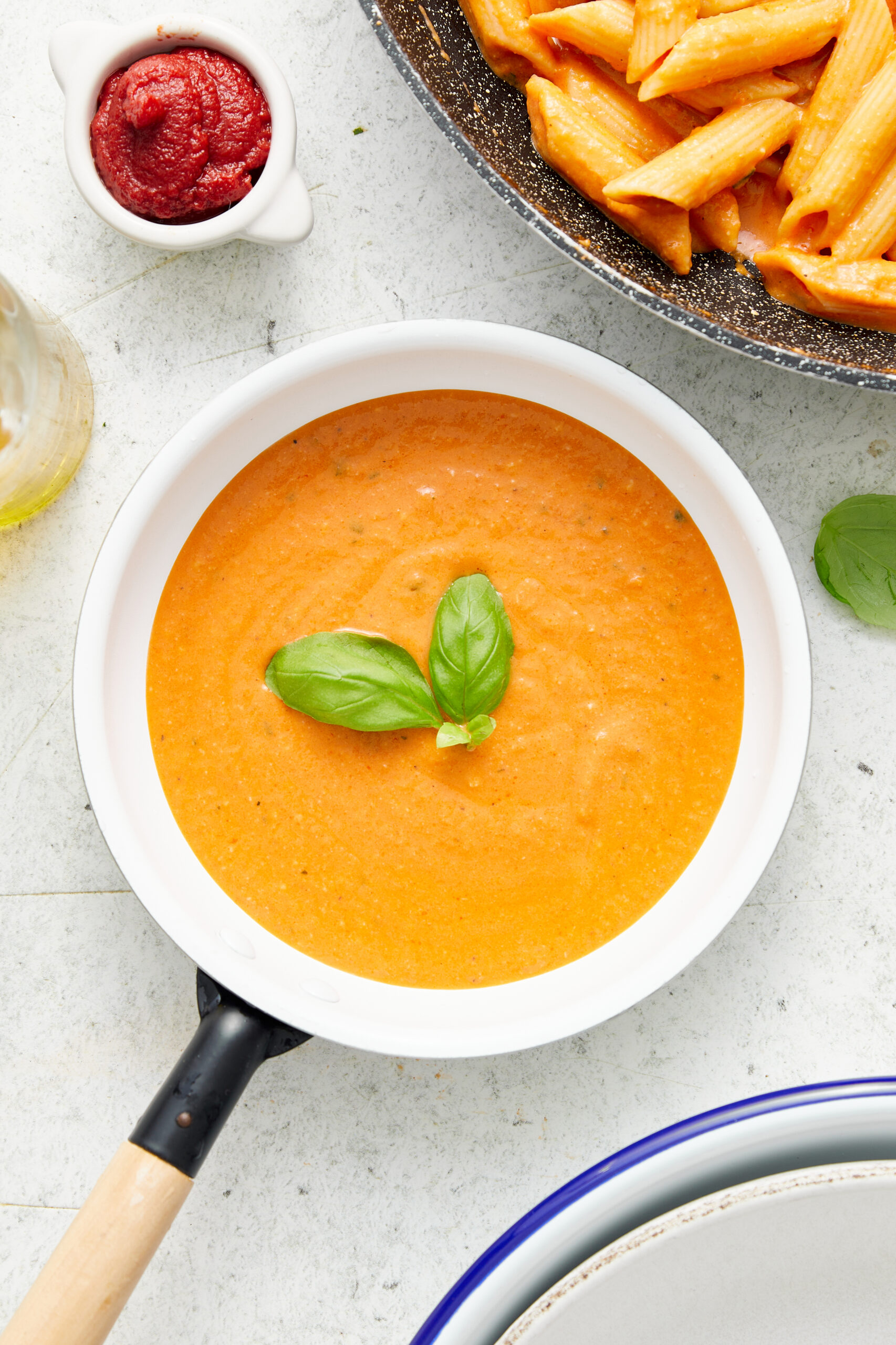 Creamy vodka sauce in a white pan, garnished with fresh basil, with penne pasta.