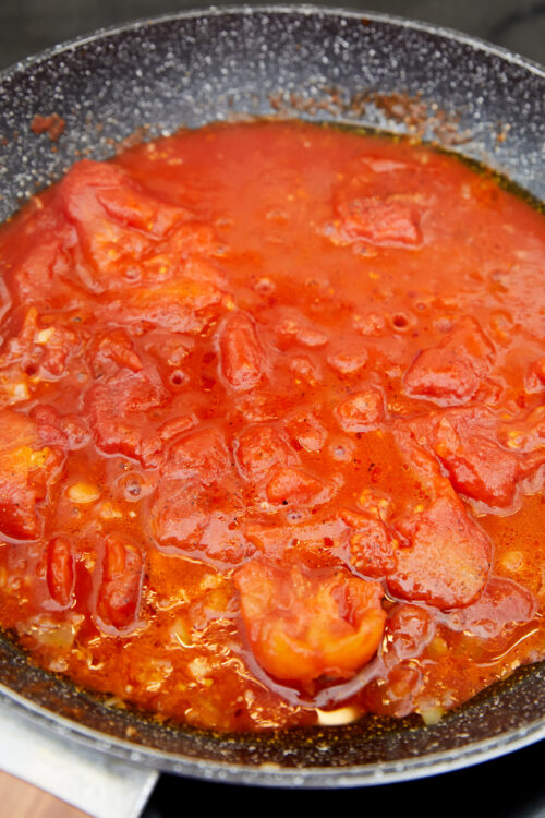 Vodka sauce simmering with whole peeled tomatoes in a skillet.